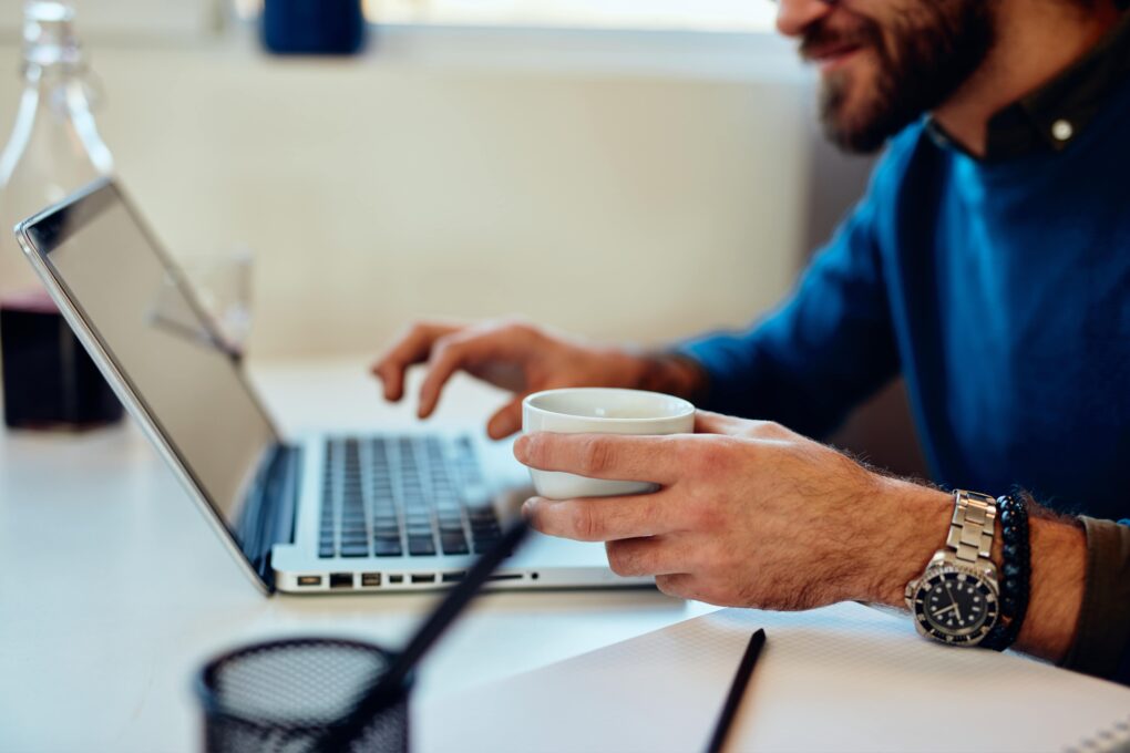 man working on his laptop holding a cup of coffee