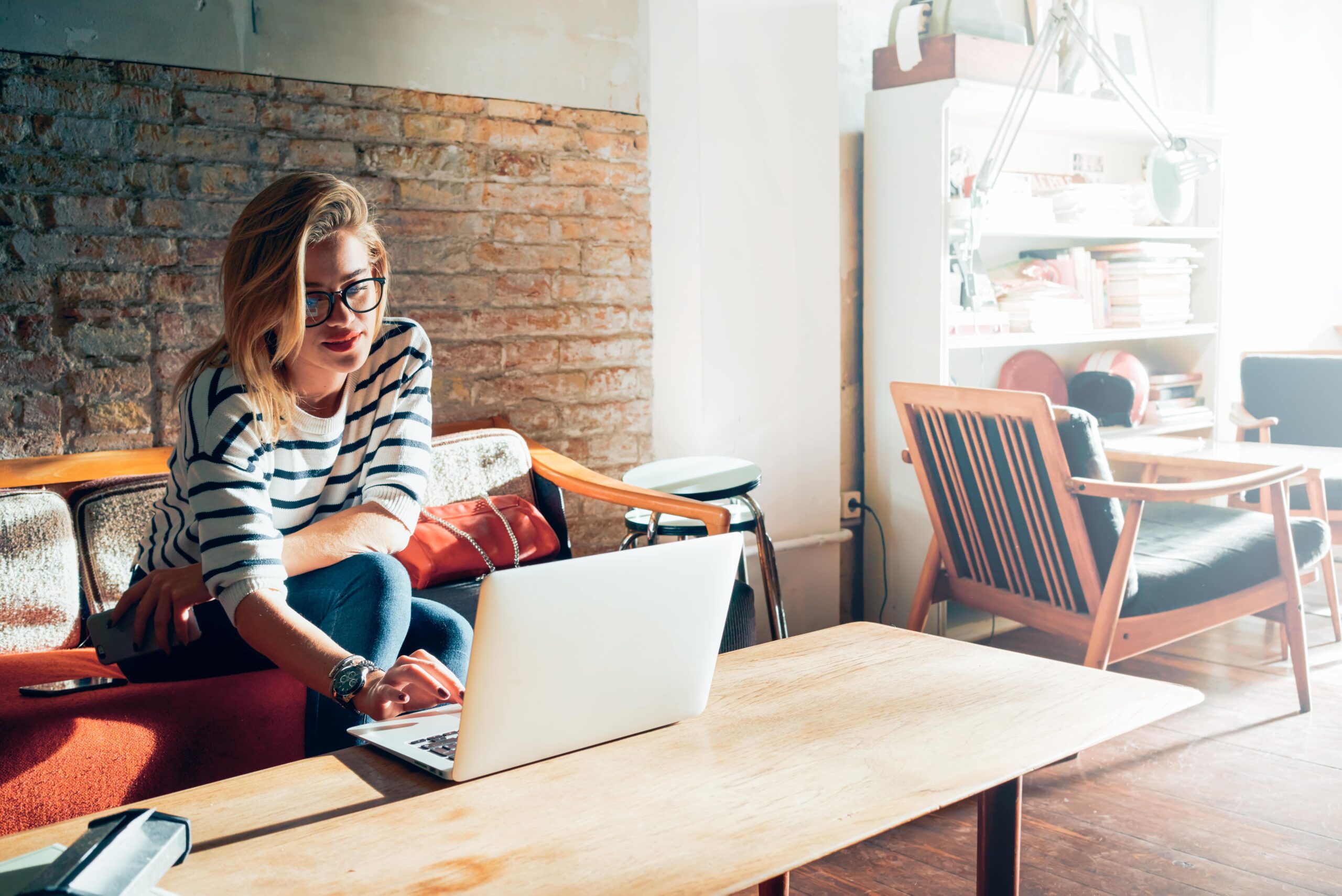 Young blonde woman sitting on a couch using her computer.