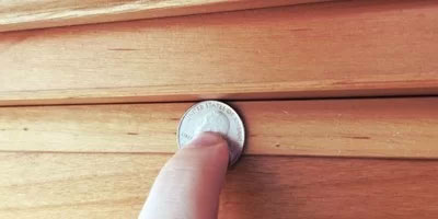 person holding a coin to a bookcase door gap
