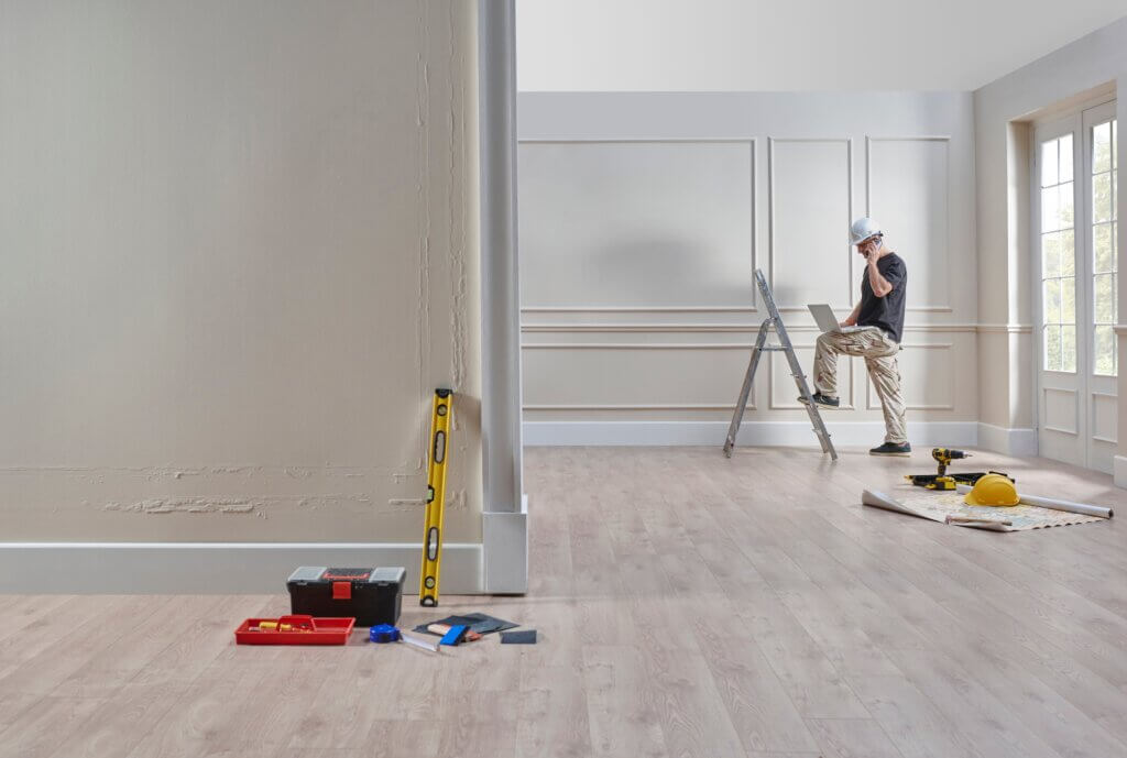 Room in progress with wall panel molding installation; tools and a construction worker on a ladder adjusting finishes.