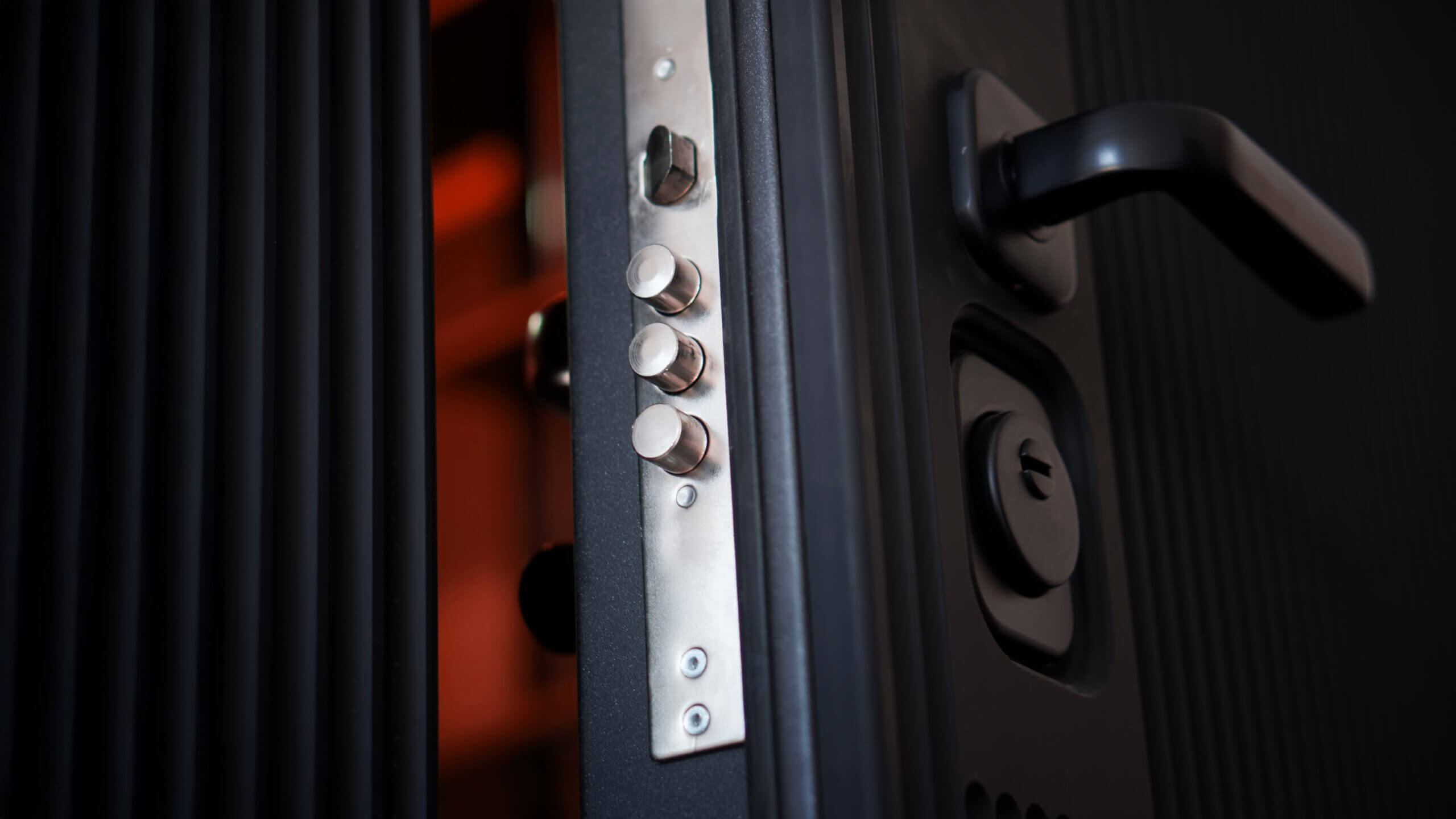 Close-up of black security door edge showing three-bolt locking system and handle detail.