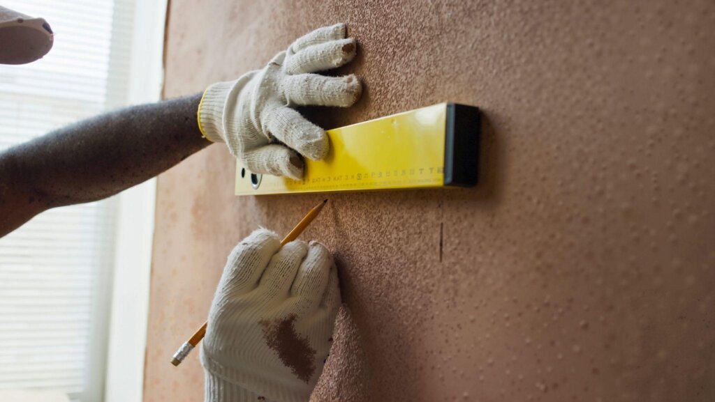 Person using a level and pencil to measure and mark a wall for installation