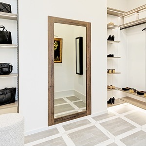 Full-length hidden mirror door seamlessly integrated into a modern luxury walk-in closet with custom shelving, light tile flooring, and concealed storage entrance.