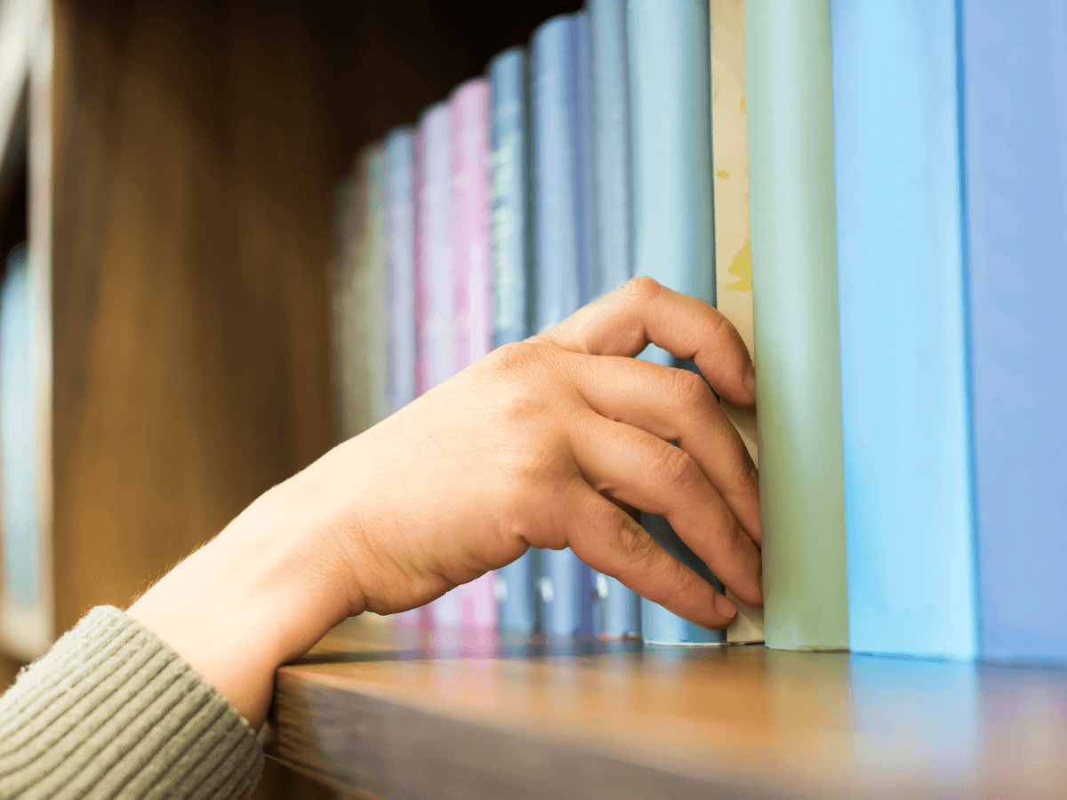 hand pulling book off bookshelf, pastel colored books